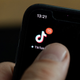A person holding a phone with the TikTok app logo in the top left.